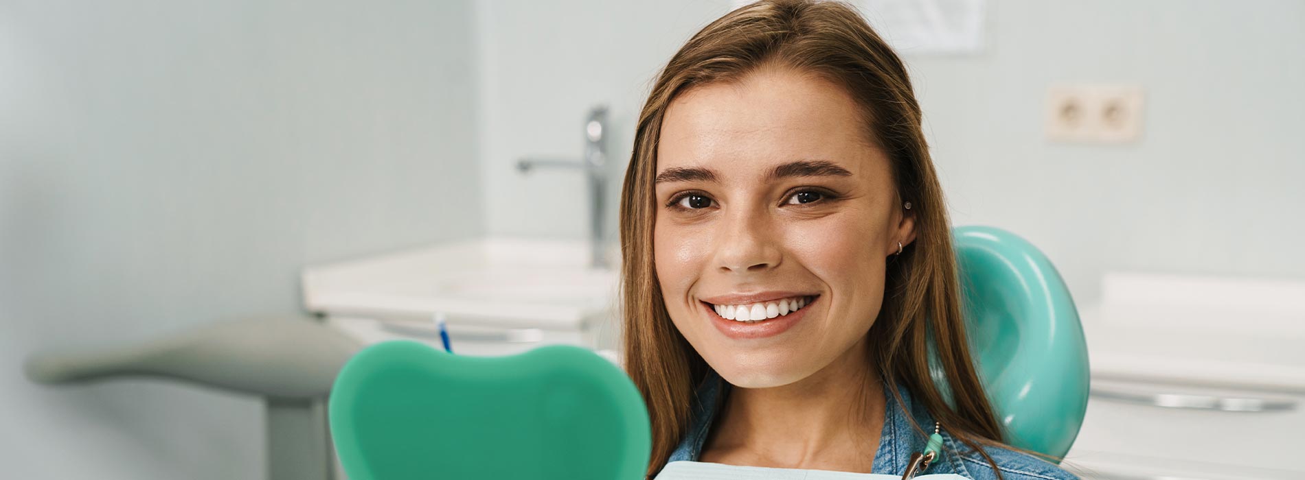 The image is a photograph of a woman with light skin, smiling at the camera. She appears to be in her late twenties or early thirties and has long hair. Her eyes are looking directly at the camera, and she is holding up her index finger near her mouth as if she s making a point or emphasizing something. The background is plain and light-colored, which suggests that this could be a stock photo used for various purposes such as advertising, personal branding, or lifestyle content.